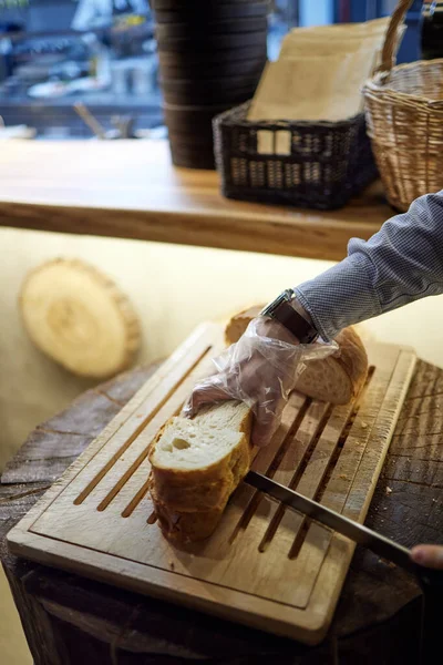 Mãos masculinas cortando pão de trigo na tábua de madeira, foco seletivo . — Fotografia de Stock