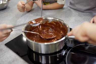 Kadın çikolatayı bir tavada eritiyor ve tereyağıyla karıştırıyor, yakın plan. Evde yemek yapmak, ev yapımı tatlı yiyecekler..