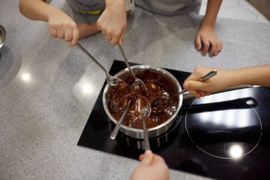 Kadın çikolatayı bir tavada eritiyor ve tereyağıyla karıştırıyor, yakın plan. Evde yemek yapmak, ev yapımı tatlı yiyecekler..