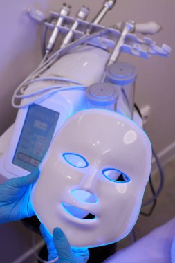 Yavaş çekimde yüz bakımı için hafif yaşlanma önleyici maske takıyordu. Özel maskeli bir kadın kanepede yatıyor. Modern güzellik ve sağlık teknolojileri.