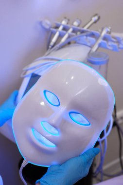 Yavaş çekimde yüz bakımı için hafif yaşlanma önleyici maske takıyordu. Özel maskeli bir kadın kanepede yatıyor. Modern güzellik ve sağlık teknolojileri.