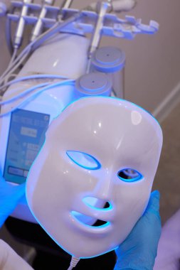 Yavaş çekimde yüz bakımı için hafif yaşlanma önleyici maske takıyordu. Özel maskeli bir kadın kanepede yatıyor. Modern güzellik ve sağlık teknolojileri.