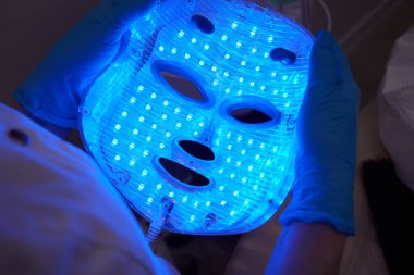 Yavaş çekimde yüz bakımı için hafif yaşlanma önleyici maske takıyordu. Özel maskeli bir kadın kanepede yatıyor. Modern güzellik ve sağlık teknolojileri.