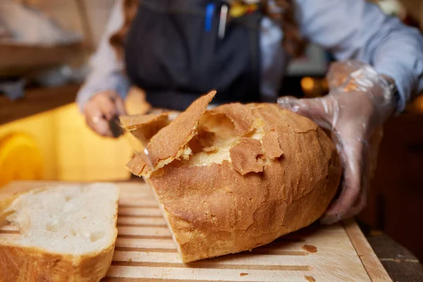 Γυναικεία χέρια κοπή σιταριού ψωμί στην ξύλινη σανίδα, επιλεκτική εστίαση. — Φωτογραφία Αρχείου