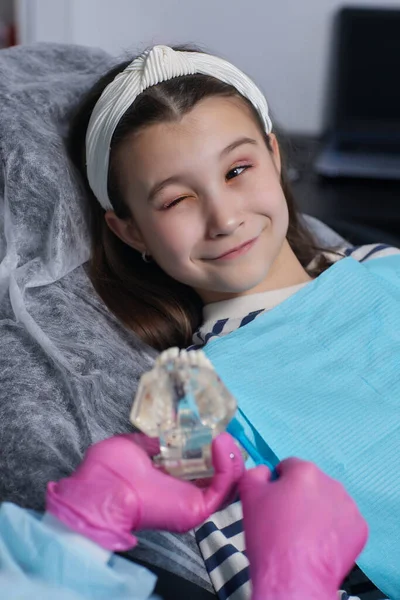 Menina limpando dentaduras de brinquedo com uma escova de dentes. — Fotografia de Stock