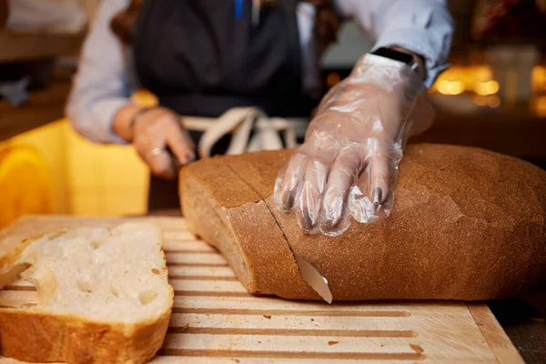 Mains féminines coupant du pain de blé sur la planche en bois, mise au point sélective. — Photo