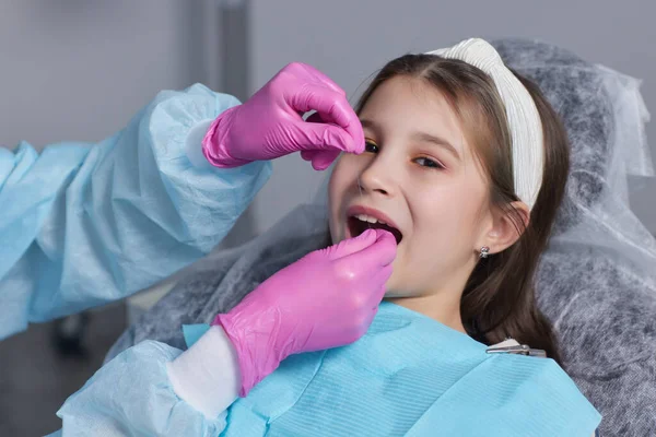 Geschnittene Hände in Latexhandschuhen, um die Vorderzähne der Kinder zu putzen. Frau hält Zahnwerkzeug neben sich. — Stockfoto