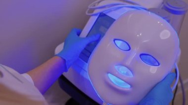 Yavaş çekimde yüz bakımı için hafif yaşlanma önleyici maske takıyordu. Özel maskeli bir kadın kanepede yatıyor. Modern güzellik ve sağlık teknolojileri.