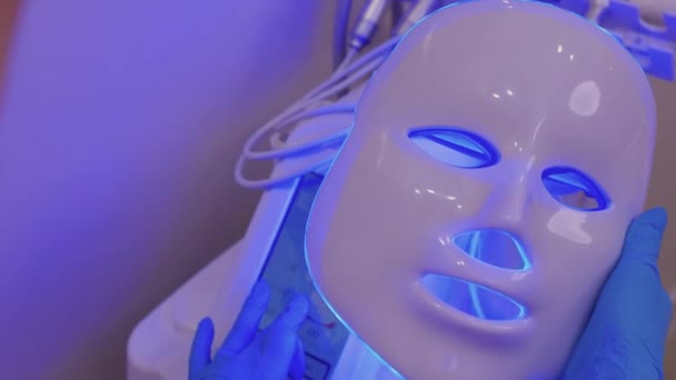 Led lätt anti-aging mask för ansiktsvård i spa slow motion. En kvinna ligger på en soffa i en speciell mask. Modern teknik för skönhet och hälsa. — Stockvideo
