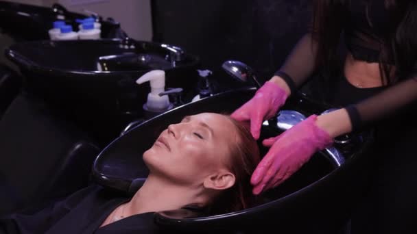 Parrucchiere nel salone di bellezza lava i capelli del suo cliente, prima della procedura di applicazione di ingredienti naturali di restauro e vitamine per capelli e taglio di capelli. — Video Stock