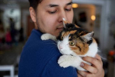 Tişörtlü genç adam elinde kedi tutuyor..