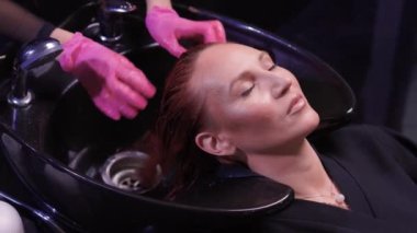 Güzellik salonundaki kuaför, saç ve saç kesimine doğal yenileme malzemeleri ve vitaminler uygulamadan önce müşterisinin saçını yıkar..