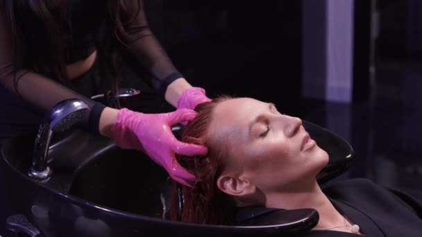 Parrucchiere nel salone di bellezza lava i capelli del suo cliente, prima della procedura di applicazione di ingredienti naturali di restauro e vitamine per capelli e taglio di capelli. — Video Stock