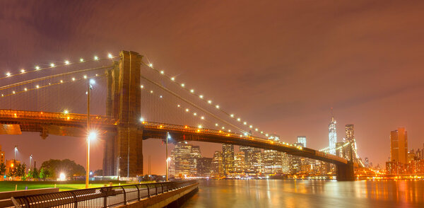 New York City night panorama with Brooklyn Bridge and illuminated downtown Manhattan business and residential buildings