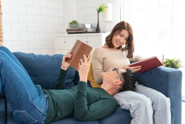 Mutlu Asyalı çift hafta sonunu evde kanepede oturup kitap okuyarak geçiriyorlar..