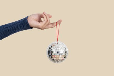 Woman holding silver christmas disco ball isolated on flesh color background. clipart