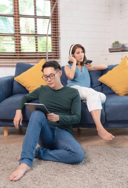 Mutlu Asyalı çift hafta sonunu evlerinde kanepede birlikte geçiriyorlar, rahatlıyor ve internet gezintisinin tadını çıkarıyorlar..