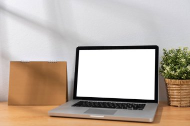 Beyaz duvar arkaplanı olan tahta masanın üzerinde boş ekran bilgisayar ve takvim Mockup.