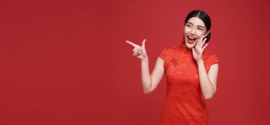 Geleneksel Cheongsam Qipao elbisesi giyen mutlu Asyalı kadın kırmızı arka planda izole edilmiş fotokopi alanını işaret ediyor. Mutlu Çin Yeni Yılı