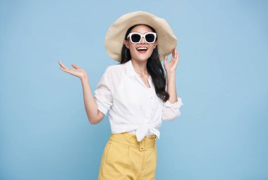 Young elegant beautiful Asian woman dressed in summer clothes smiling and pointing to empty copy space isolated on blue background.
