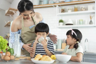 Mutlu Asyalı anne ve oğlu ve kızı sabah mutfakta süt bardakları tutuyor. Aile aktivitelerinin tadını çıkarın..