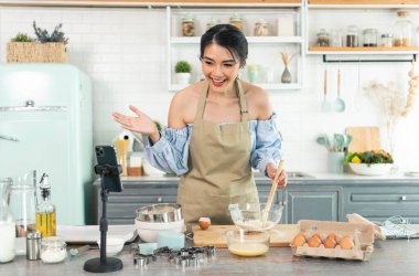 Asyalı kadın yemek blogcusu akıllı telefon kamerasının önünde pasta pişirirken video kaydediyor ve mutfakta canlı yayın yapıyor.. 
