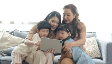Happy Asian family using digital tablet in living at home, relaxing at home for lifestyle concept.