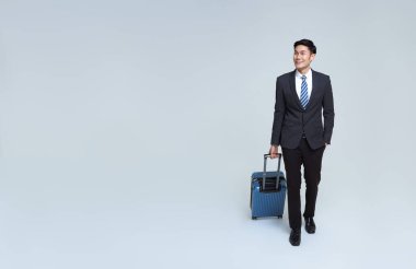Yakışıklı Asyalı işadamı boş bir havaalanında stüdyo beyaz arka planda izole edilmiş bir bavulla yürüyor..