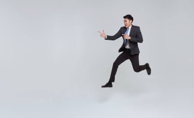 Yakışıklı, mutlu, enerjik, genç Asyalı iş adamı havada zıplıyor ve beyaz fotokopi arkaplanındaki izole edilmiş yeri işaret ediyor..