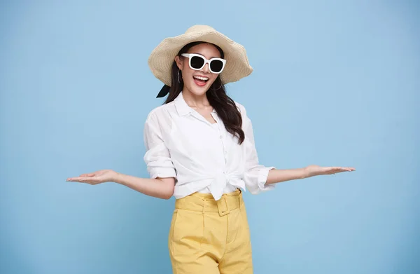 Happy beautiful Asian woman dressed in summer clothes smiling with open hand gesture of welcome isolated on blue background