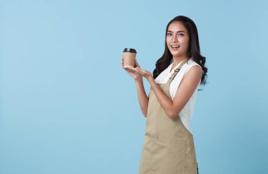 Önlüklü genç Asyalı girişimci kadın elinde bir fincan kahveyle mavi arka planda izole edilmiş. Barista ve garson servisi konsepti