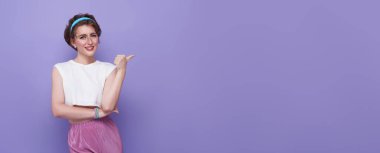 Mor arka planda fotokopi ile izole edilmiş parmağını gösteren mutlu genç bir kadın.