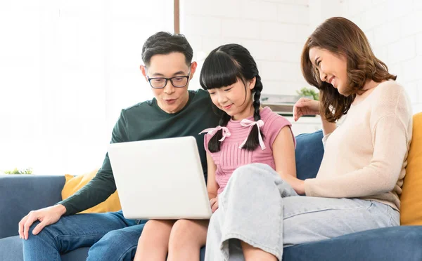Happy Asian family using computer laptop together on sofa at home living room.