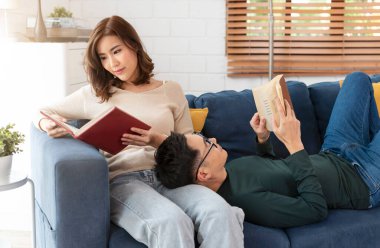 Mutlu Asyalı çift hafta sonunu evde kanepede oturup kitap okuyarak geçiriyorlar..