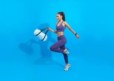 Go to training fitness. Happy Asian sporty woman with bag running on blue background. Sports and healthy lifestyle