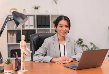 Executive Asian businesswoman sitting on desk in office.
