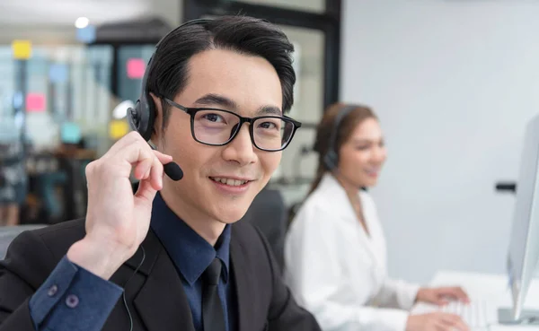 Asian call center agent team, customer service support wearing headset or headphone talking with customer in modern office.