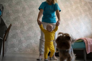 Anne küçük oğlana yürümeyi öğretiyor.