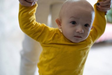 Anne küçük oğlana yürümeyi öğretiyor.