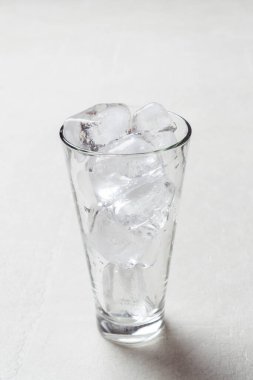 Aydınlık bir masanın üzerindeki bardakta buzla dolu uzun bir bardak, yakın plan.