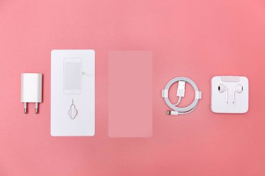 Modern akıllı telefon aksesuarları ve pembe arka planda kulaklıklar.