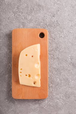 Gri beton arka planda büyük delikleri olan bir parça Maasdam peyniri. Yakın plan.
