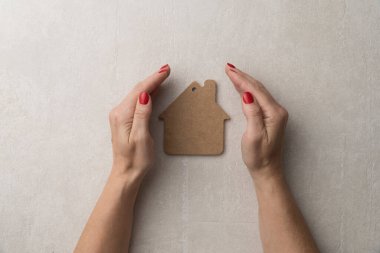 Ev için koruma ve sevgi kavramı. Düz bir ahşap ev modeli, kadın eli.