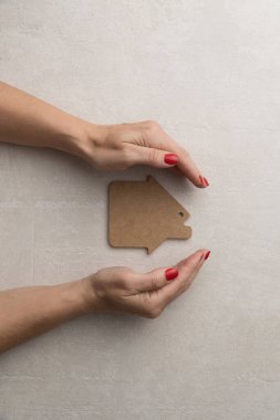Ev için koruma ve sevgi kavramı. Düz bir ahşap ev modeli, kadın eli.