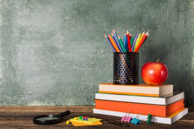 Okul yönetim kurulunun arka planında bir yığın kitap, kırtasiye ve kırmızı elma var. Eğitim ve okul konseptine dönüş.