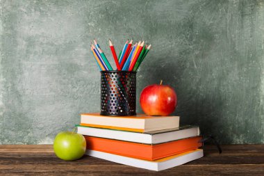 Bir yığın kitap, ofis malzemeleri ve okul yönetim kurulunun arka planında iki elma. Eğitim ve okul konseptine dönüş.