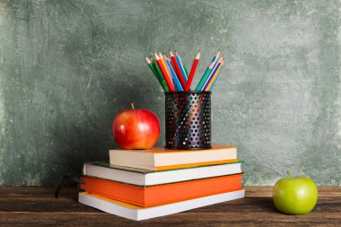 Bir yığın kitap, ofis malzemeleri ve okul yönetim kurulunun arka planında iki elma. Eğitim ve okul konseptine dönüş.