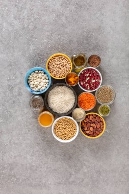Gri beton arka planda vejetaryen gıda ve diyet kavramı, baklagiller, tohumlar ve renkli kaselerde fotokopi alanı ile gruplandırılmış tahıllar