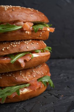 Karanlık bir mutfak masasında somon balığı ve roka ile yakın plan bir sandviç.