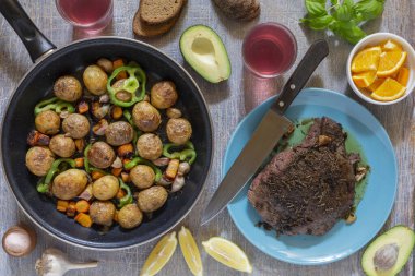 Ev yapımı yemekler, sebzeler, otlar, tavada kızarmış biftek ve yeni patateslerle dolu bir yemek masası.
